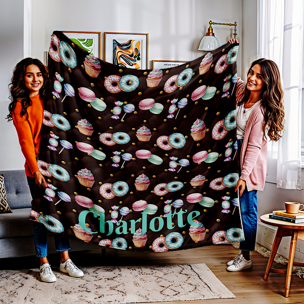 Two women holding a chocolate colour throw blanket with colourful donut and cupcake pattern in a living room.