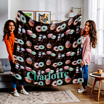 Two women holding a chocolate colour throw blanket with colourful donut and cupcake pattern in a living room.