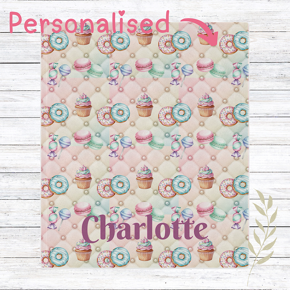 Personalised pink Throw blanket patterned  with donuts, cupcakes, and candies on a wooden surface.