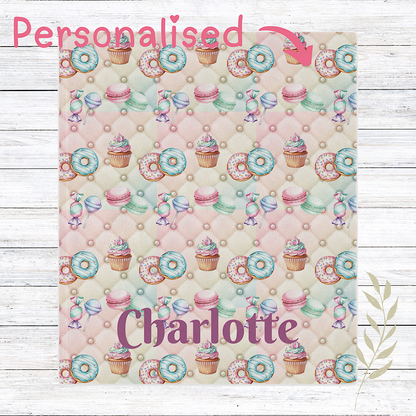 Personalised pink Throw blanket patterned  with donuts, cupcakes, and candies on a wooden surface.