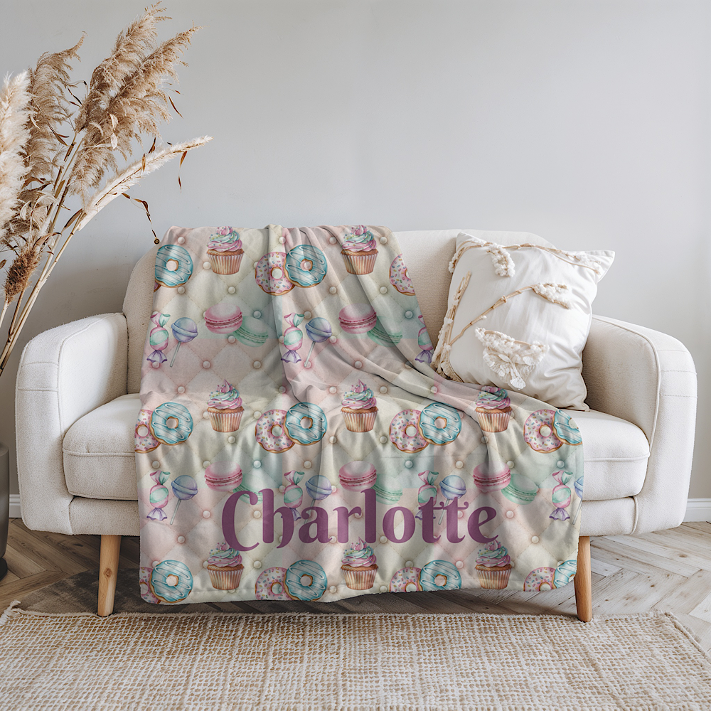Personalised pink throw Blanket with cupcake pattern on a white couch.